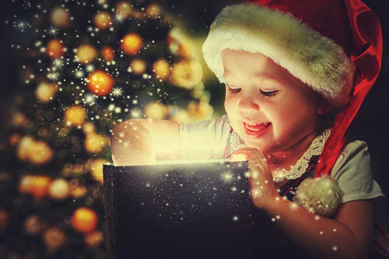Young child opening a present that is glowing with light. Christmas tree in the background.